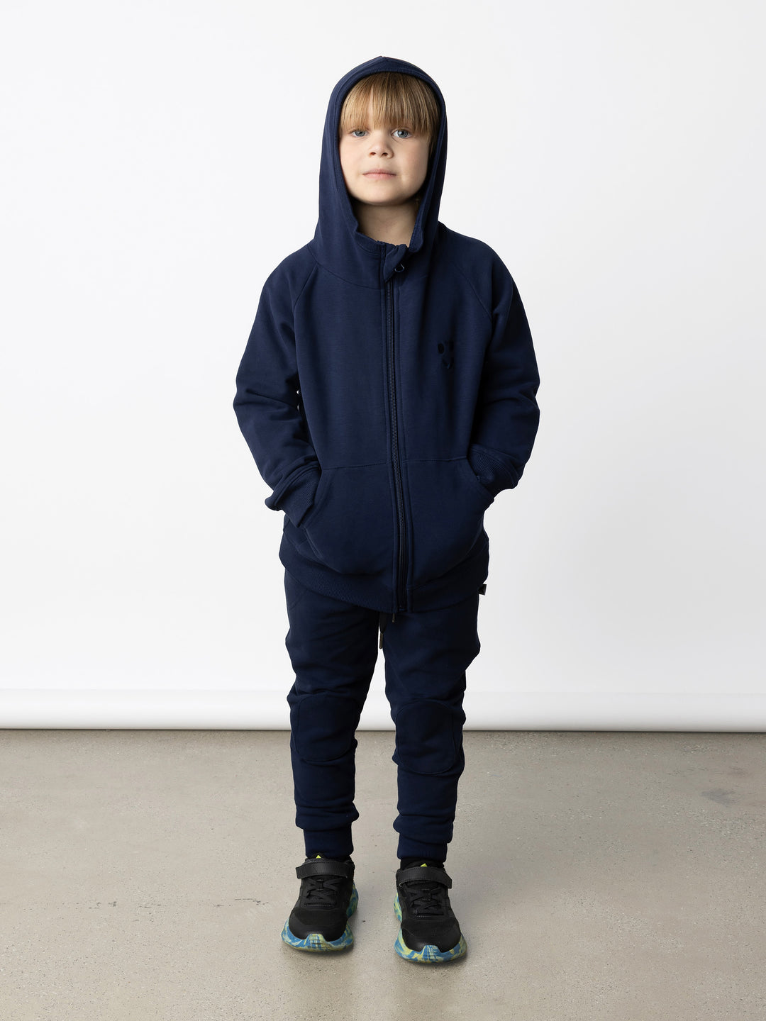 Minti kids clothing. Cosy zip through hoodie with kangaroo pockets for extra warmth! 2x2 rib trim on the hood, cuffs and hem. Small tonal Happy Face embroidery on the front. 330 Gram // Brushed Inside // 95% Cotton // 5% Elastane.