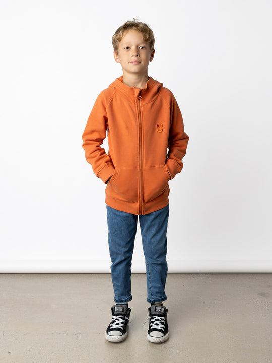 Minti kids clothing. Cosy zip through hoodie with kangaroo pockets for extra warmth! 2x2 rib trim on the hood, cuffs and hem. Small tonal Happy Face embroidery on the front. 330 Gram // Brushed Inside // 95% Cotton // 5% Elastane.