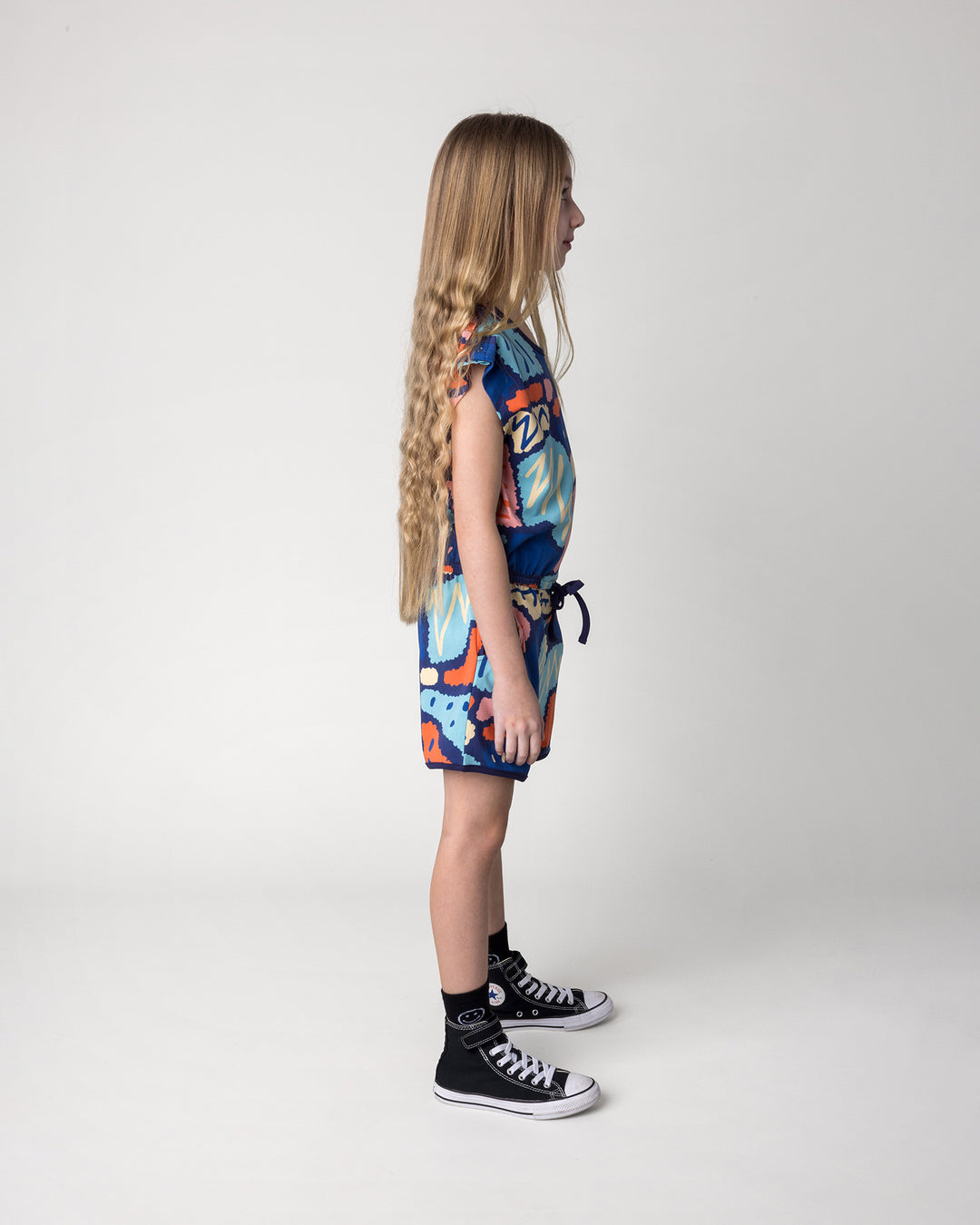 Kid wearing the Cool Shapes Playsuit in dark blue, side view