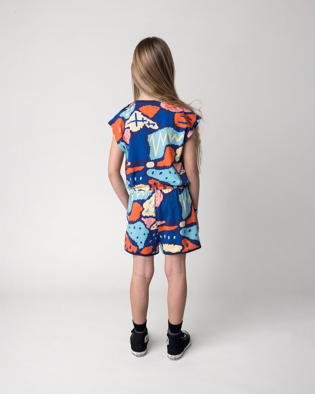 Kid wearing the Cool Shapes Playsuit in dark blue, back view
