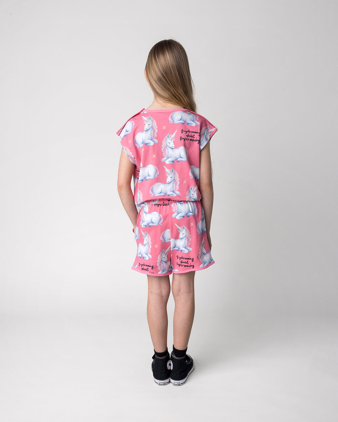 Kid wearing the Daydreaming Unicorn Playsuit in candy, back view