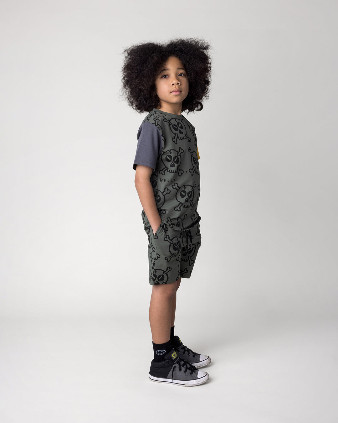 Kid wearing the Hello Skull Short in forest with the Hello Skull Tee in forest, dark grey and yellow, side view