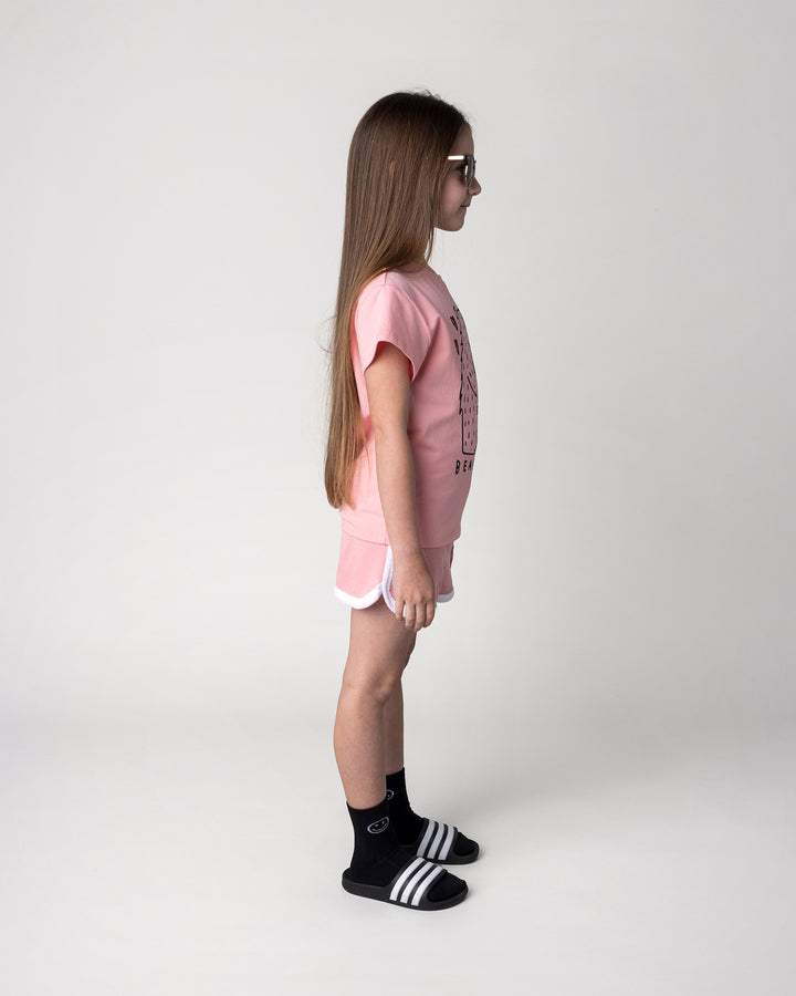 Kid wearing the Bear Hug Tee in pink with the Track Star Short in pink, side view