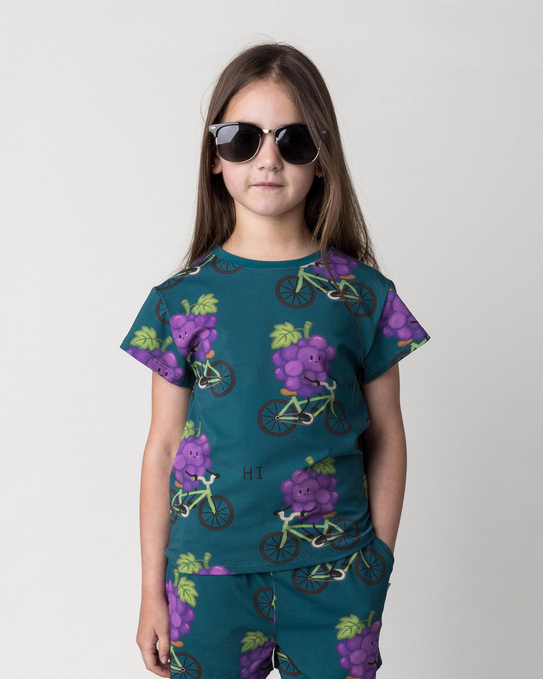 Close up of the Biking Grape Tee in dark teal on a kid, front view