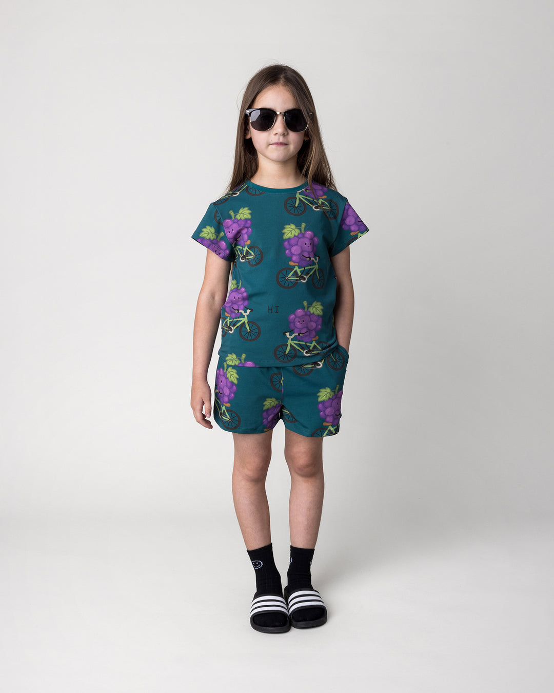 Kid wearing the Biking Grape Tee in dark teal with the Biking Grape Short in dark teal, front view