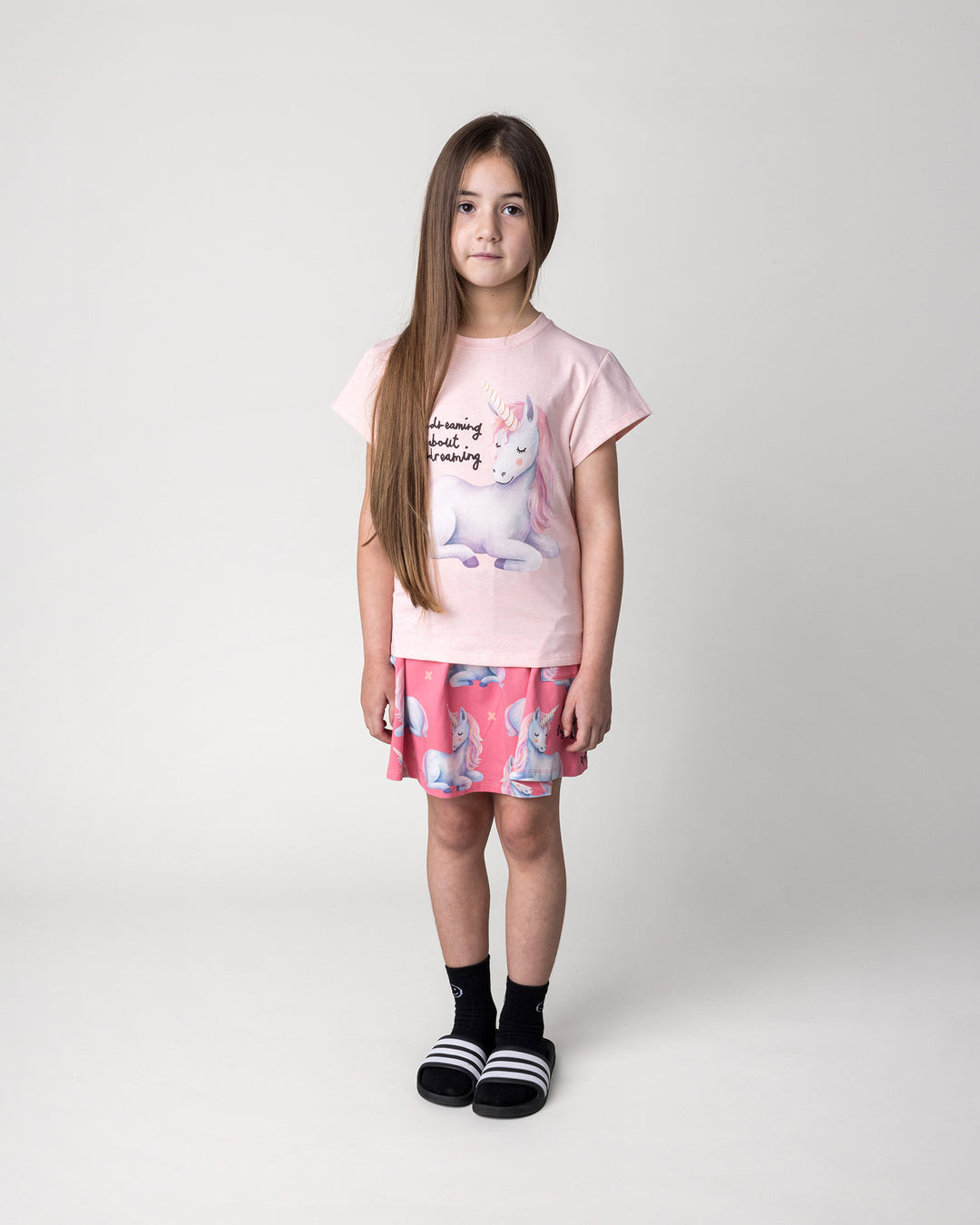 Kid wearing the Daydreaming Unicorn Tee in pink marle with the Daydreaming Unicorn Skirt in candy, front view