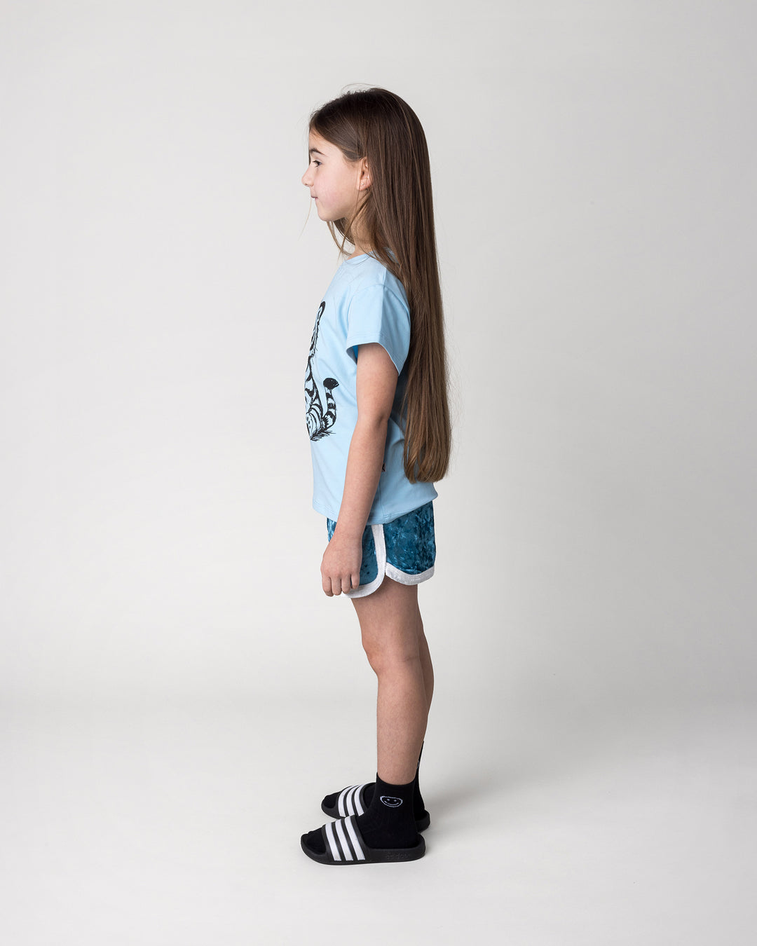 Kid wearing the Happy Tiger Tee in light blue with the Velvet Runner Short in light blue and cream, side view