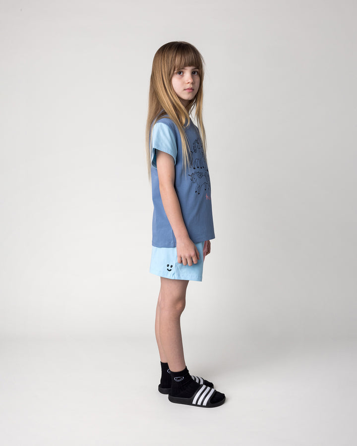Kid wearing the Hello Unicorns Tee in mid blue, light blue and pink with the Two Tone Short in light blue and pink, side view