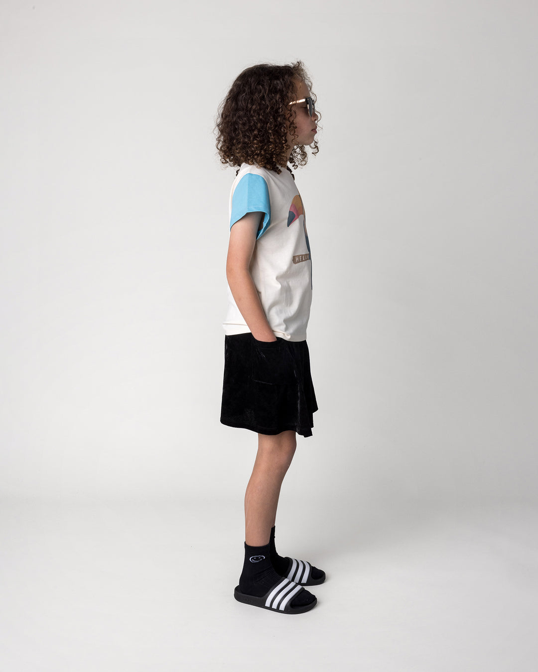 Kid wearing the Hello Toucan Tee in cream, pink and aqua with the Velvet Skirt in black, side view