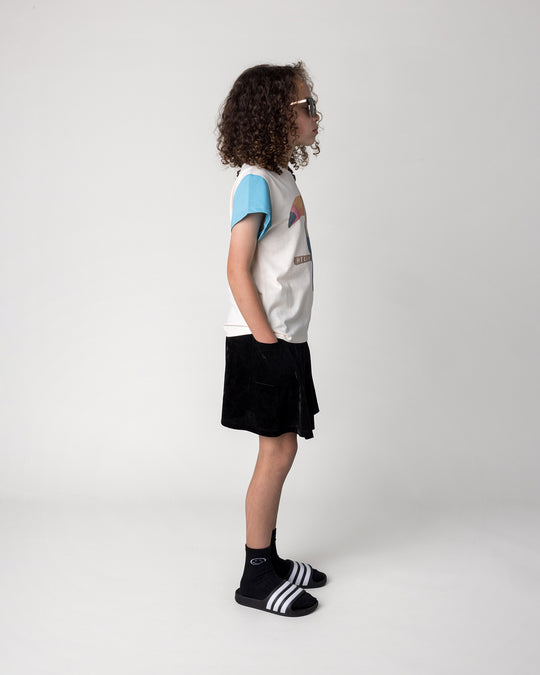 Kid wearing the Hello Toucan Tee in cream, pink and aqua with the Velvet Skirt in black, side view