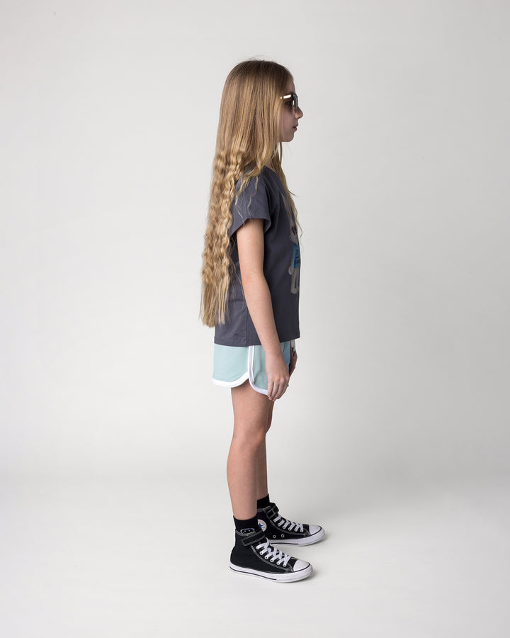 Kid wearing the Icecream Bunny Tee in dark grey with the Sprint Short in mint, aqua and lilac, side view