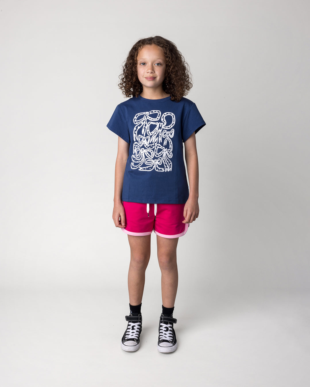 Kid wearing the Messy Bows Tee in ink with the Sprint Short in crimson and pink, front view