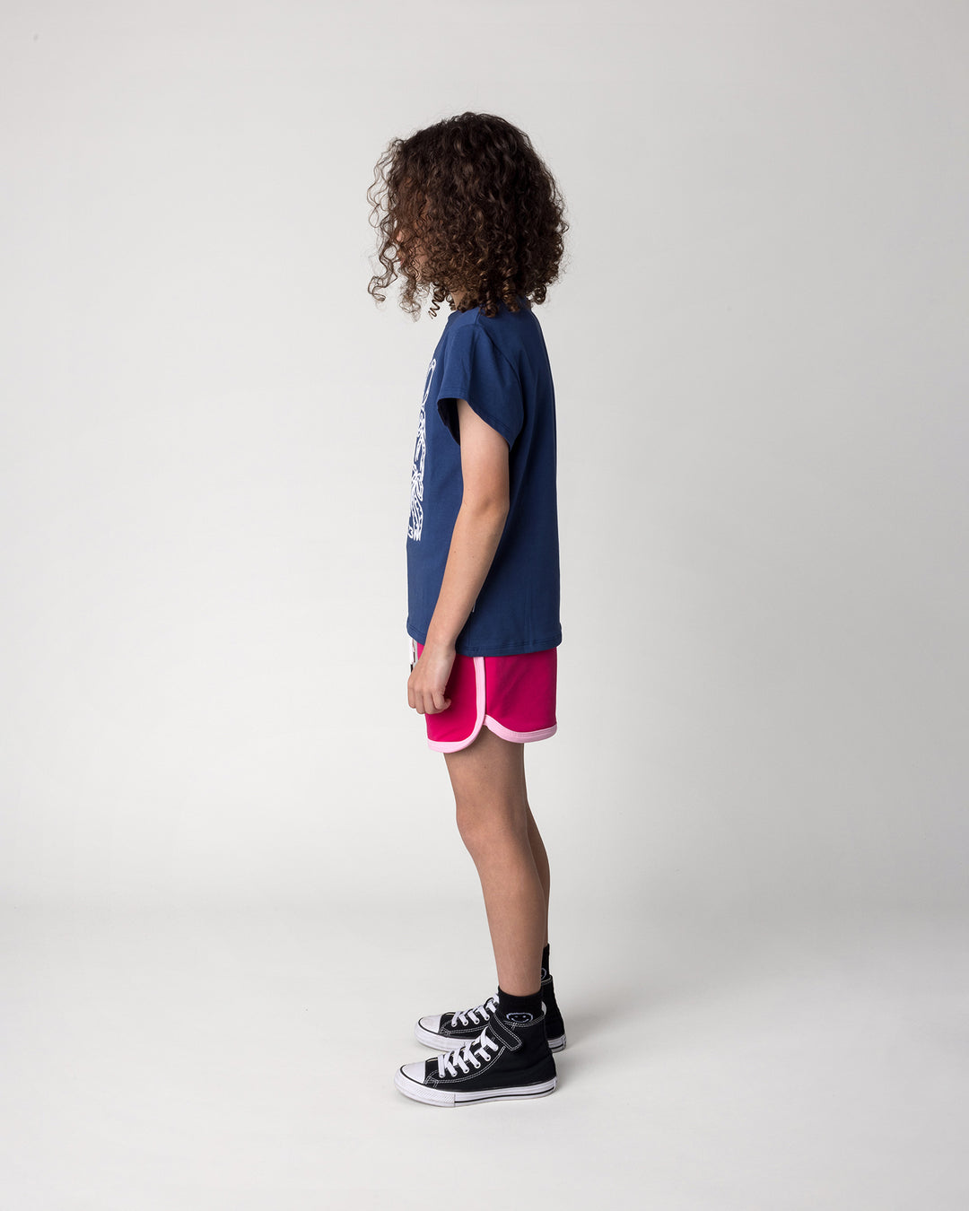 Kid wearing the Messy Bows Tee in ink with the Sprint Short in crimson and pink, side view