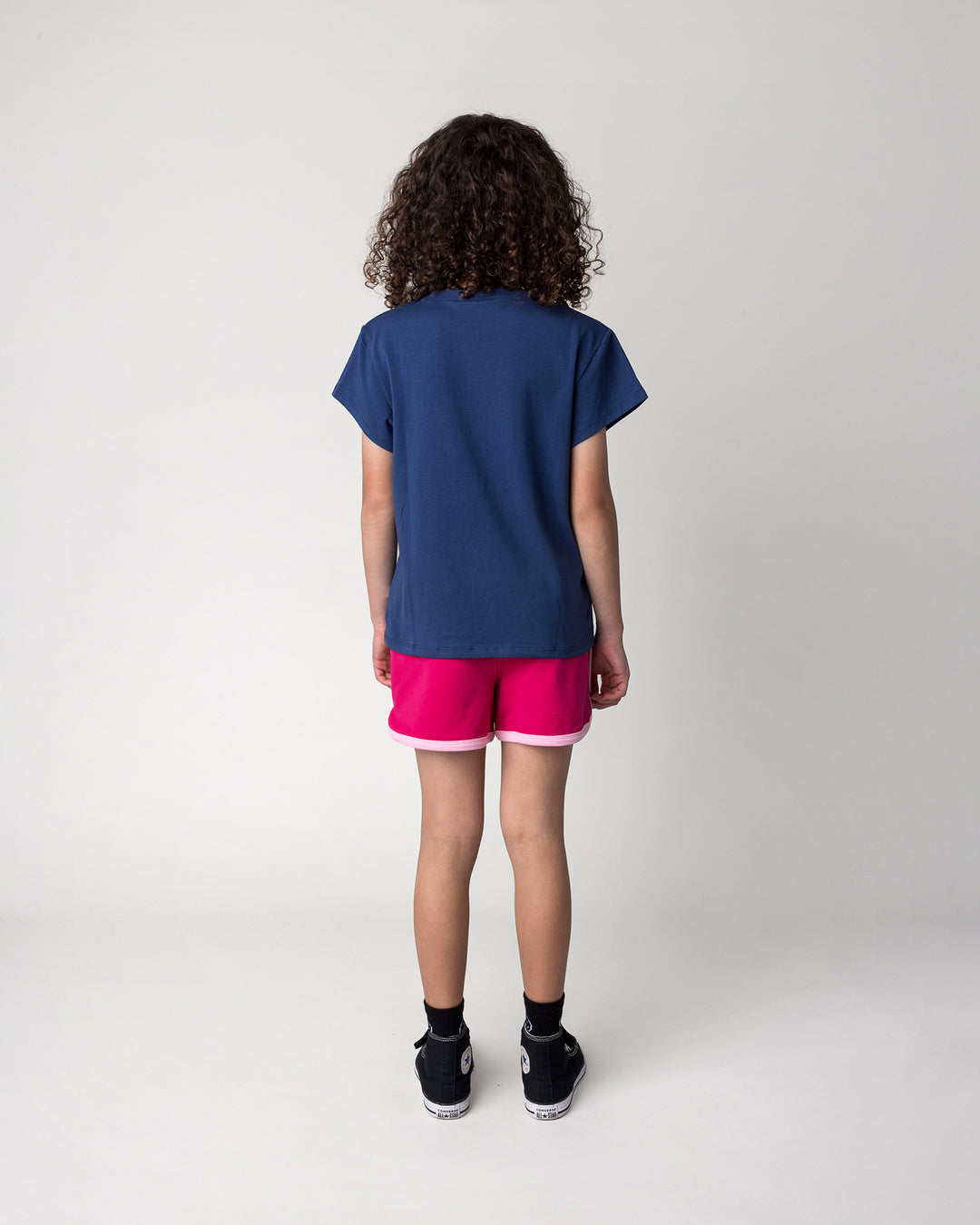 Kid wearing the Messy Bows Tee in ink with the Sprint Short in crimson and pink, back view