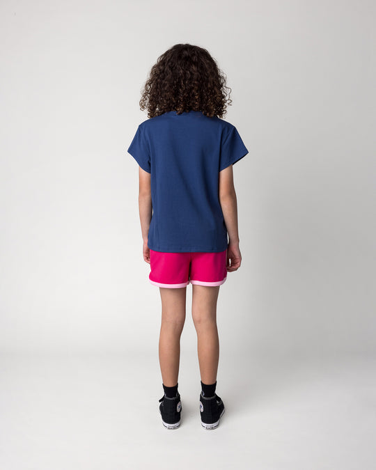 Kid wearing the Messy Bows Tee in ink with the Sprint Short in crimson and pink, back view