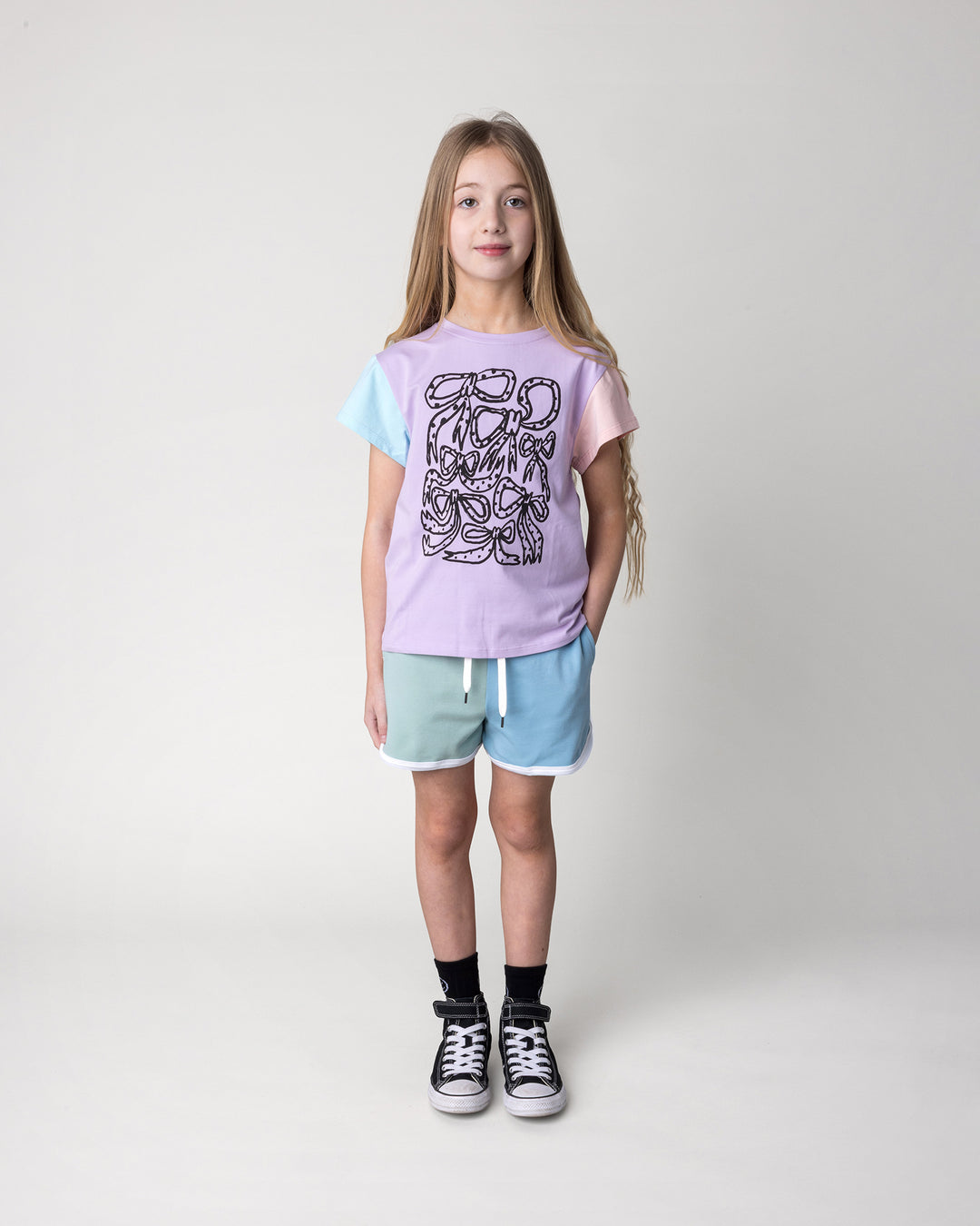Kid wearing the Messy Bows Tee in lilac, aqua and pink with the Sprint Short in mint, aqua and lilac, front view
