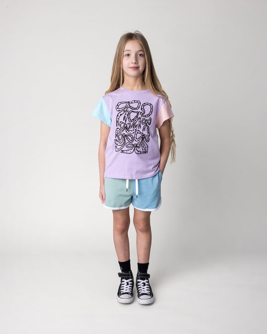 Kid wearing the Messy Bows Tee in lilac, aqua and pink with the Sprint Short in mint, aqua and lilac, front view