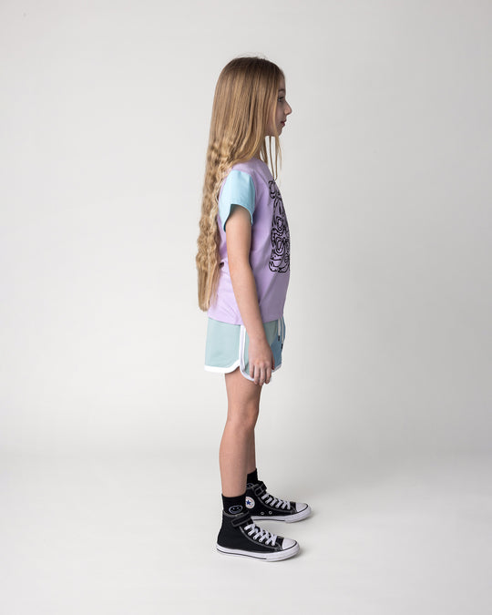Kid wearing the Messy Bows Tee in lilac, aqua and pink with the Sprint Short in mint, aqua and lilac, side view