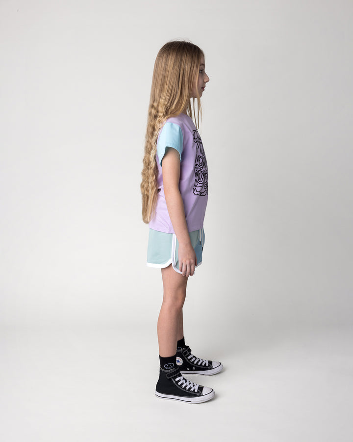 Kid wearing the Messy Bows Tee in lilac, aqua and pink with the Sprint Short in mint, aqua and lilac, side view