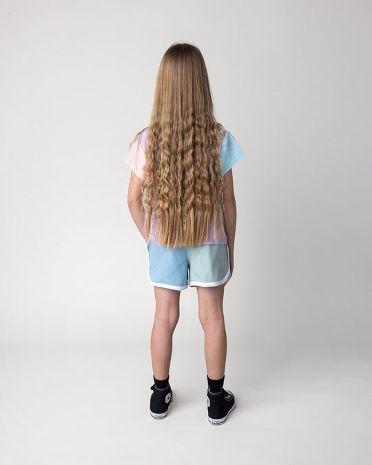 Kid wearing the Messy Bows Tee in lilac, aqua and pink with the Sprint Short in mint, aqua and lilac, back view