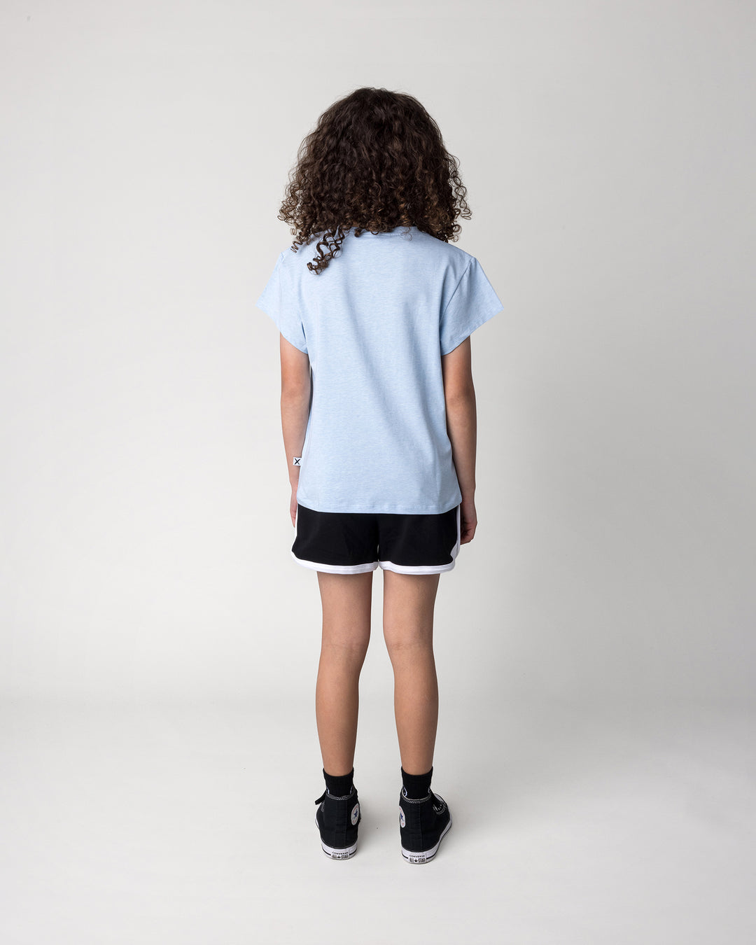 Kid wearing the Skate Puppy Tee in light blue marle with the Sprint Short in black and white, back view