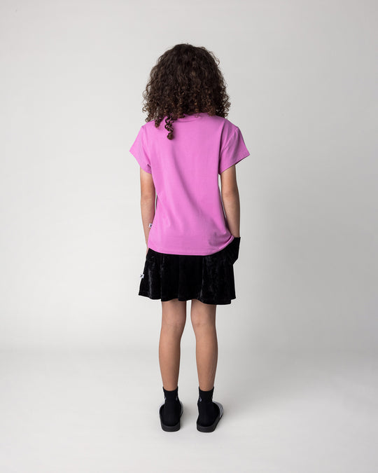 Kid wearing the Stay Cool Tee in violet with the Velvet Skirt in black, back view
