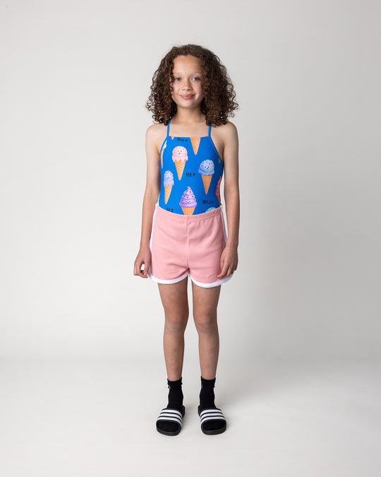 Kid wearing the Happy Icecreams Swimsuit in bright blue with the Track Star Short in pink, front view