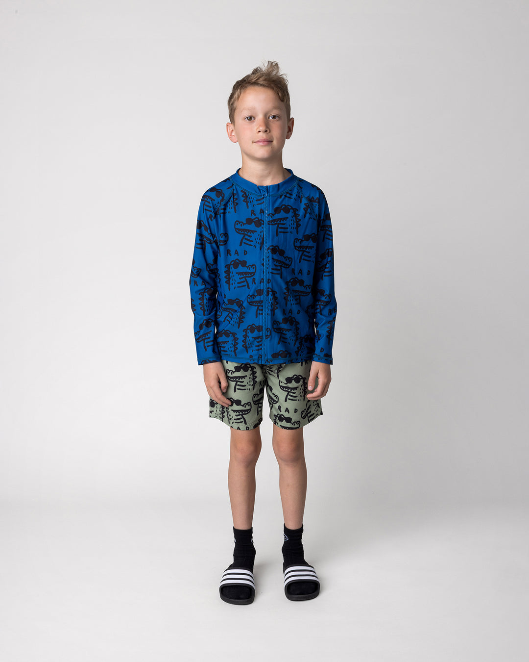Kid wearing the Rad Croc Boardies in khaki with the Rad Croc Rashie in midnight, front view