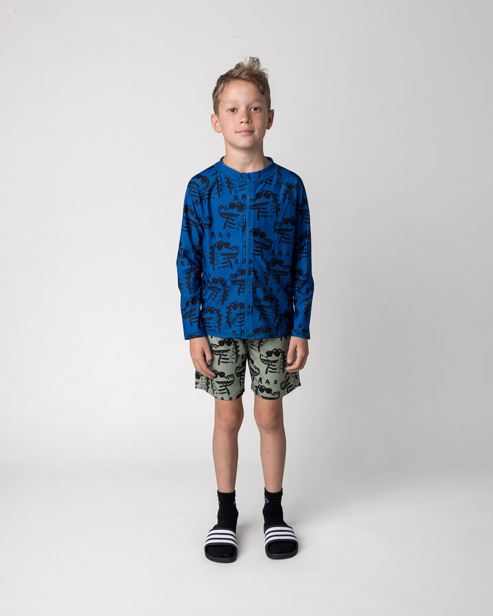 Kid wearing the Rad Croc Boardies in khaki with the Rad Croc Rashie in midnight, front view