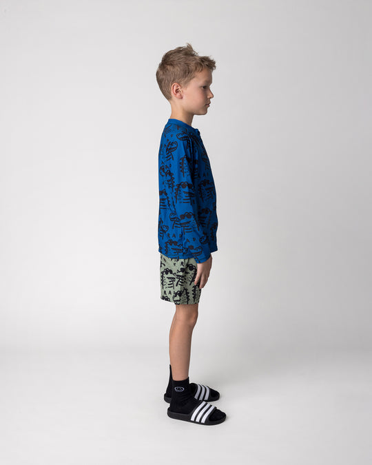 Kid wearing the Rad Croc Boardies in khaki with the Rad Croc Rashie in midnight, side view