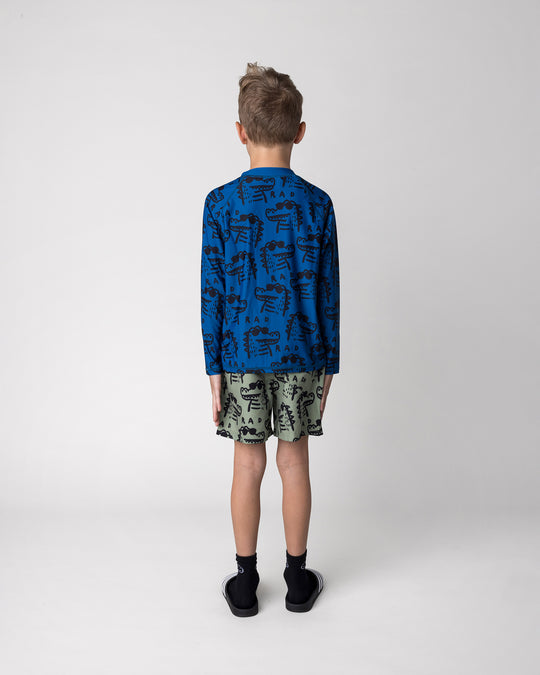 Kid wearing the Rad Croc Boardies in khaki with the Rad Croc Rashie in midnight, back view