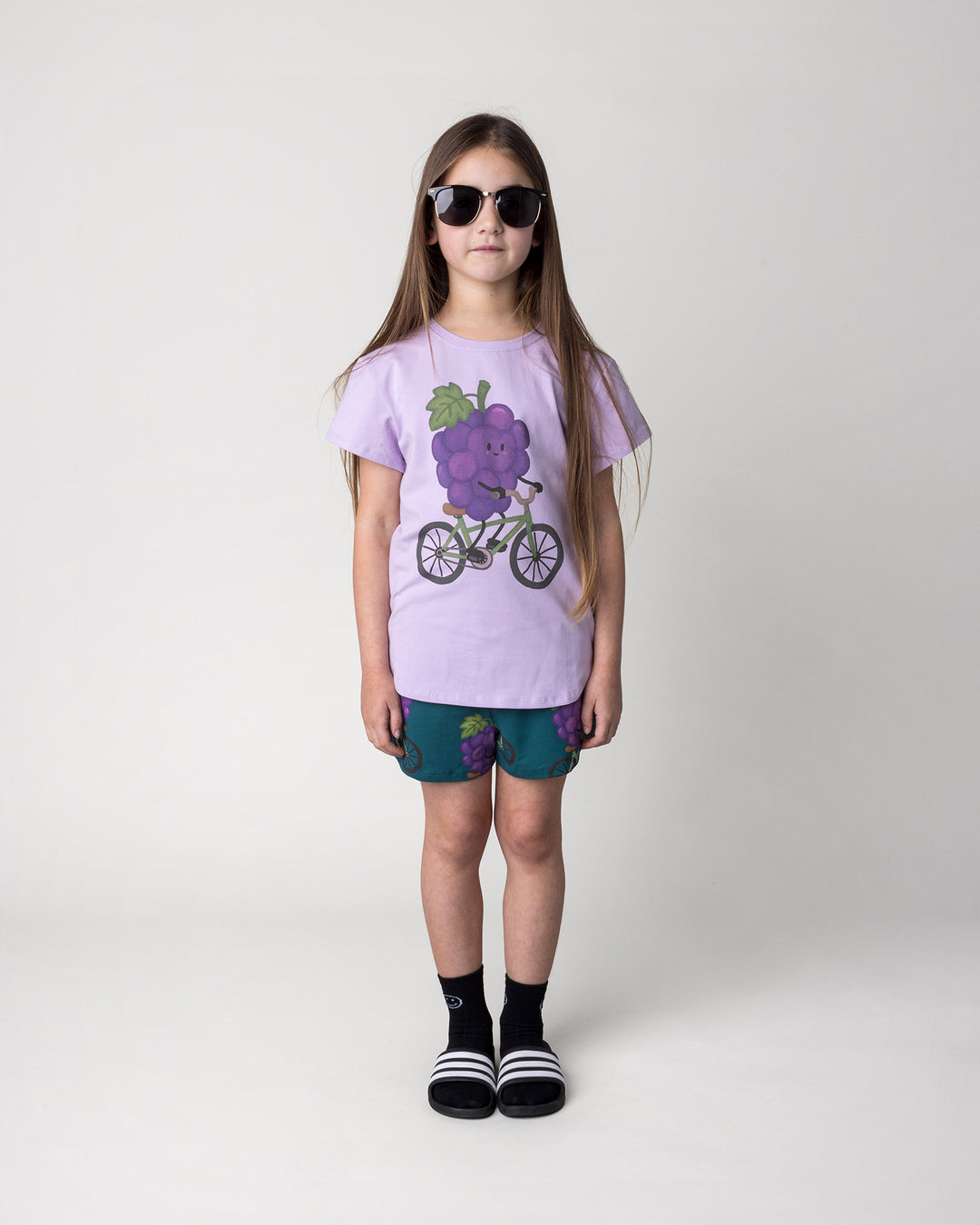 Kid wearing the Biking Grape Tee in lilac with the Biking Grape Short in dark teal, front view