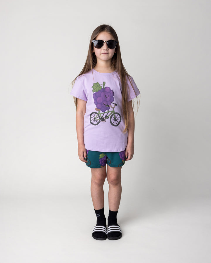 Kid wearing the Biking Grape Tee in lilac with the Biking Grape Short in dark teal, front view