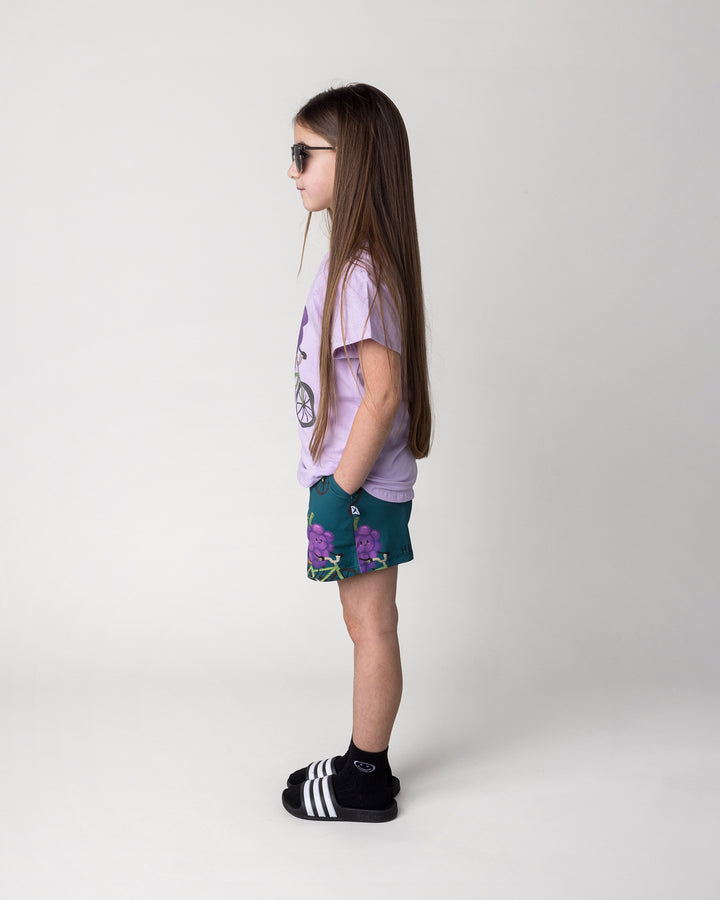 Kid wearing the Biking Grape Tee in lilac with the Biking Grape Short in dark teal, side view