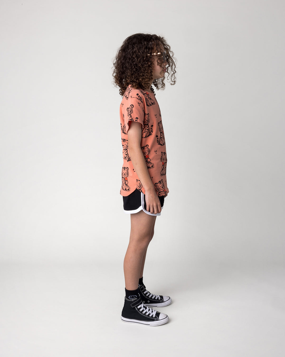 Kid wearing the Happy Tiger Tee in apricot with the Sprint Short in black and white, side view