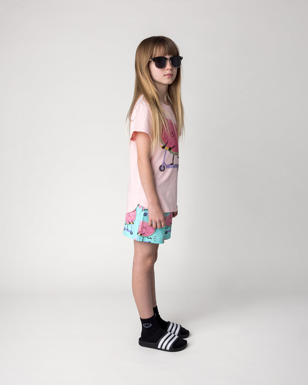 Kid wearing the Scooting Watermelon Tee in light pink with the Scooting Watermelon Short in light mint, side view
