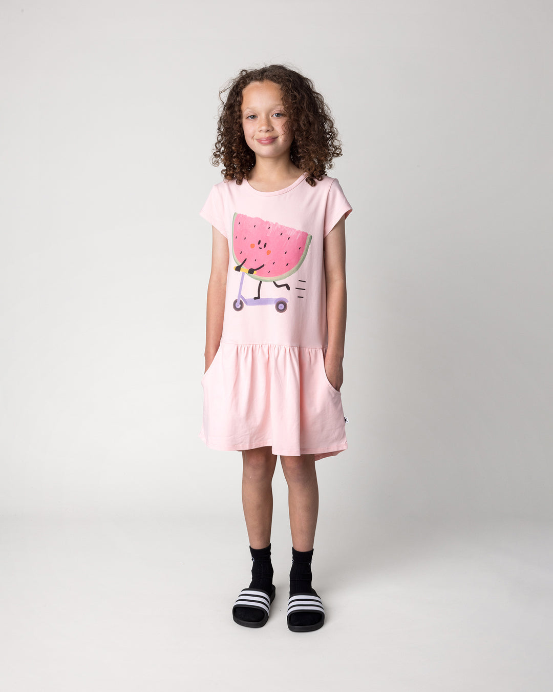 Kid wearing the Scooting Watermelon Dress in light pink, front view