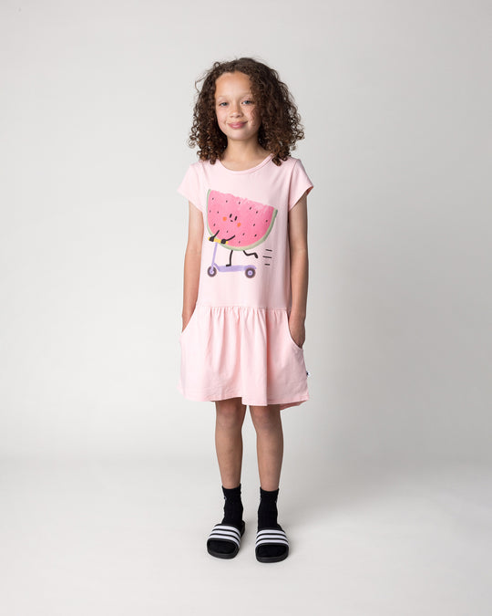 Kid wearing the Scooting Watermelon Dress in light pink, front view