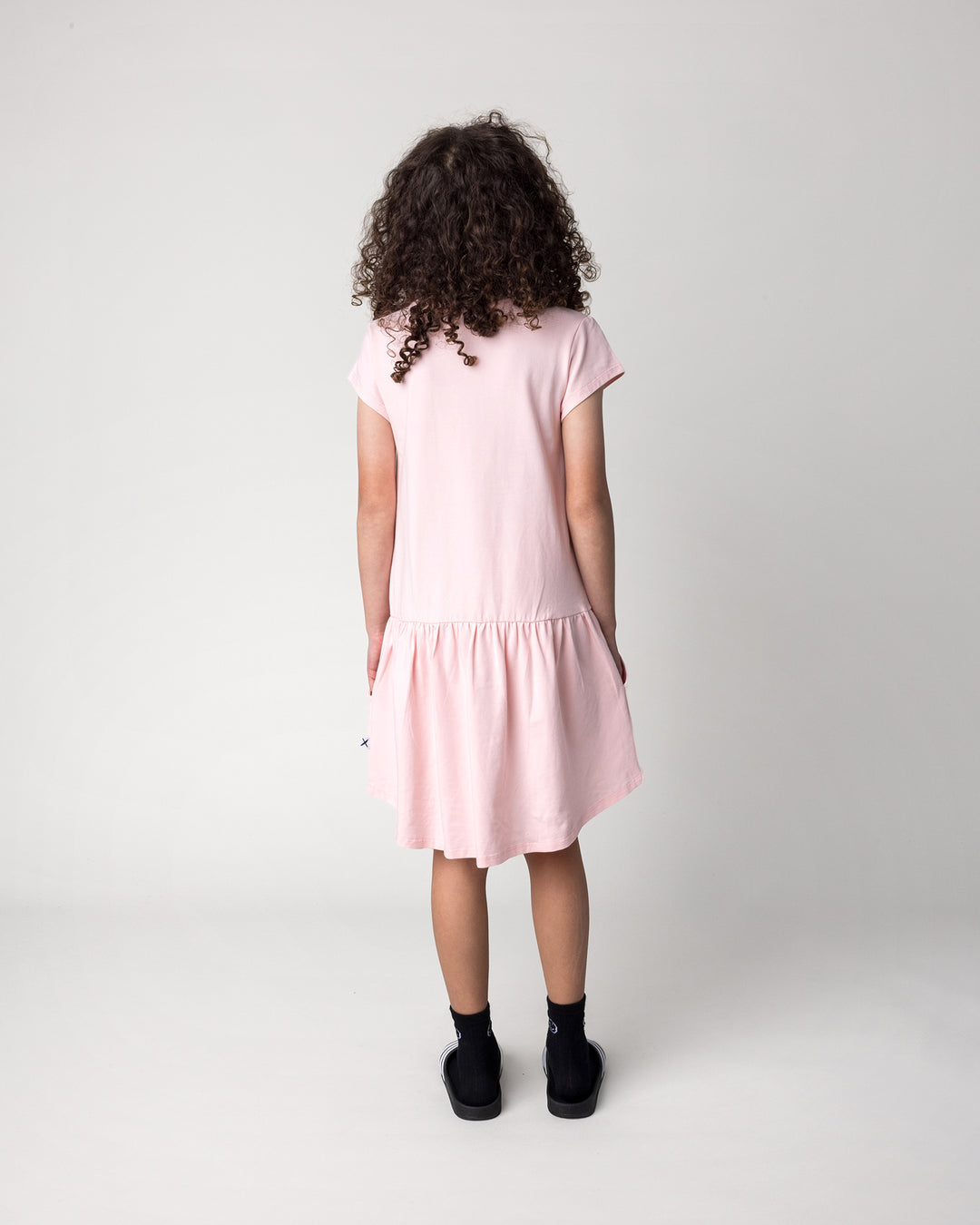 Kid wearing the Scooting Watermelon Dress in light pink, back view