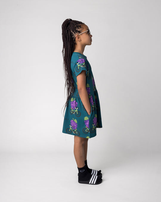 Kid wearing the Biking Grape Dress in dark teal, side view