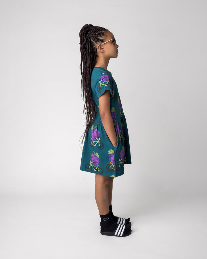 Kid wearing the Biking Grape Dress in dark teal, side view