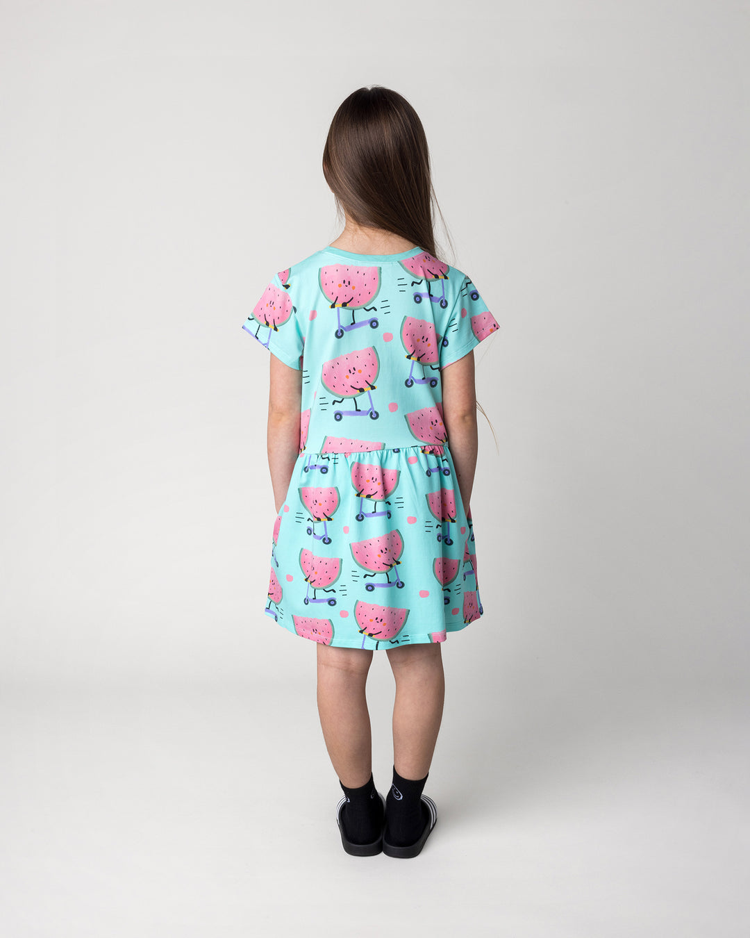 Kid wearing the Scooting Watermelon Dress in light mint, back view