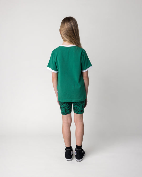 Kid wearing the Big Flowers Bike Pant in kelly green with the Flower Party Tee in kelly green and white, back view