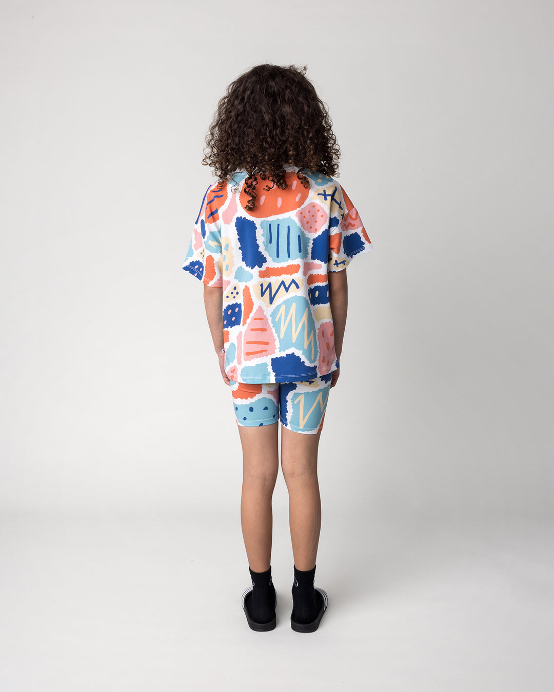 Kid wearing the Cool Shapes Bike Pant in white with the Cool Shapes Tee in white, back view