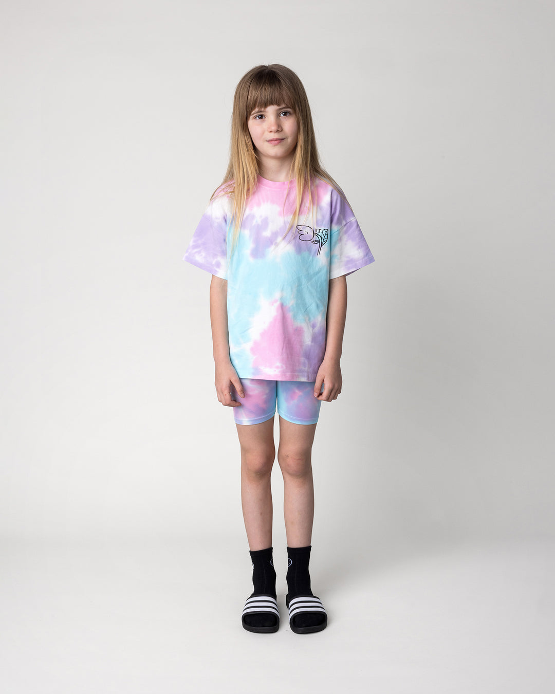 Kid wearing the Tie Dye Bike Pant in multi with the Pocket Flower Tee in tie dye, front view