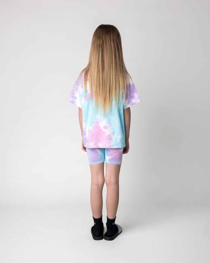 Kid wearing the Tie Dye Bike Pant in multi with the Pocket Flower Tee in tie dye, back view