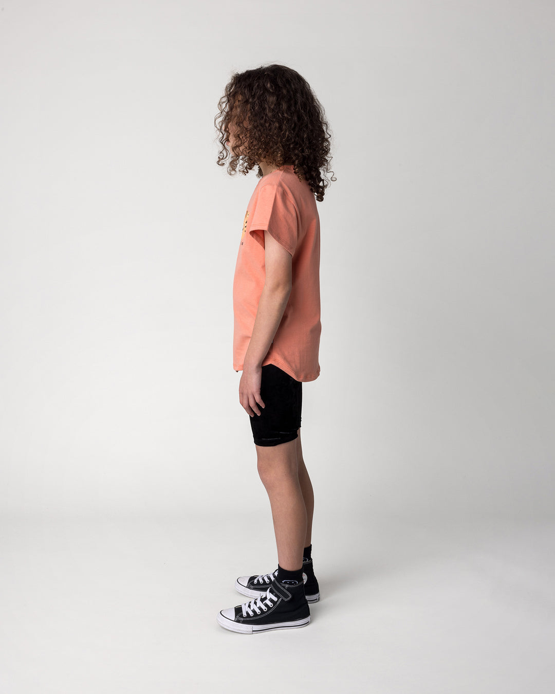 Kid wearing the Velvet Bike Pant in black with the Hello Tiger Tee in apricot, side view