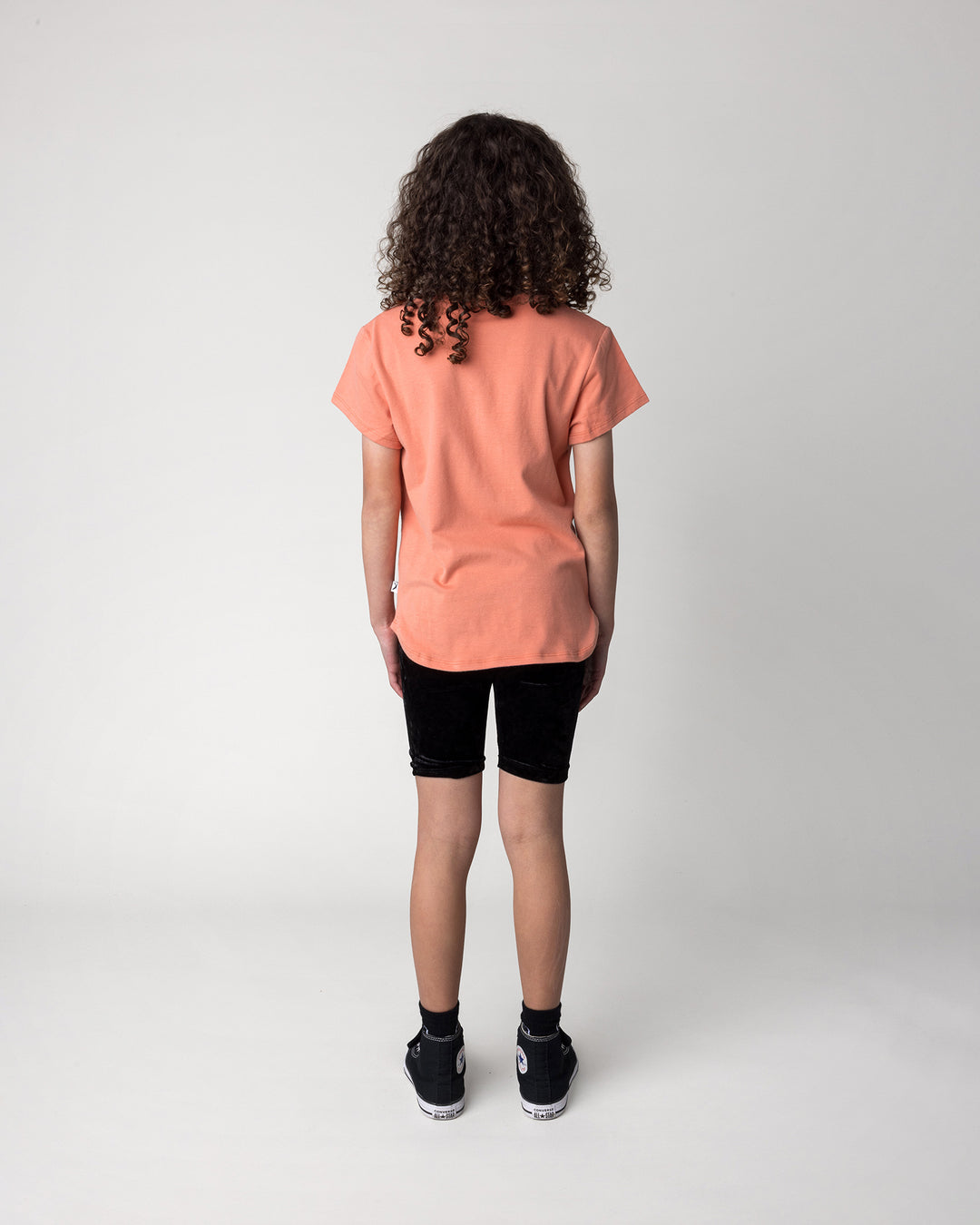 Kid wearing the Velvet Bike Pant in black with the Hello Tiger Tee in apricot, back view