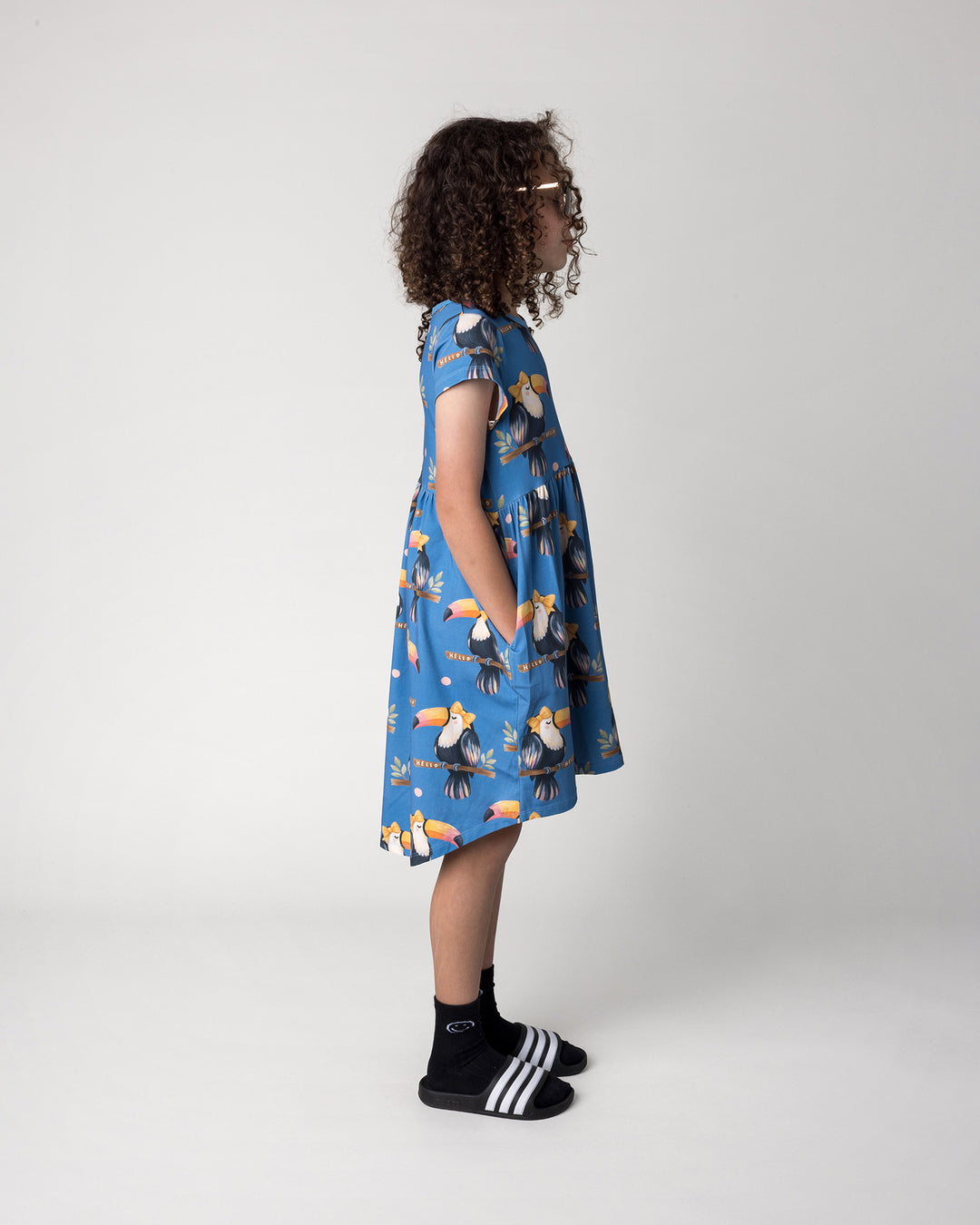 Kid wearing the Hello Toucan Dress in aqua, side view