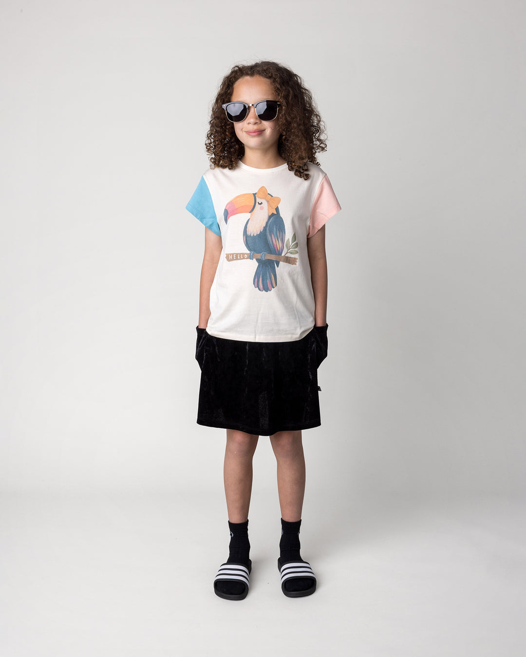Kid wearing the Velvet Skirt in black with the Hello Toucan Tee in cream, pink and aqua, front view